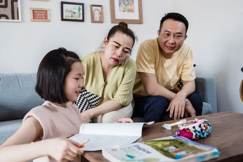 A parent sitting with a child at a table, helping her work through a homework worksheet
